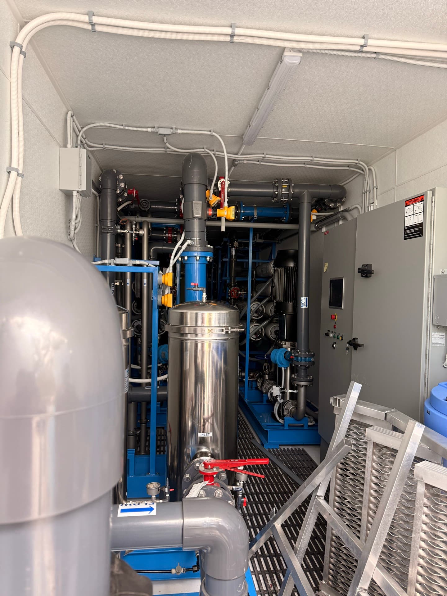 Industrial water treatment facility with blue piping and stainless steel pressure vessels