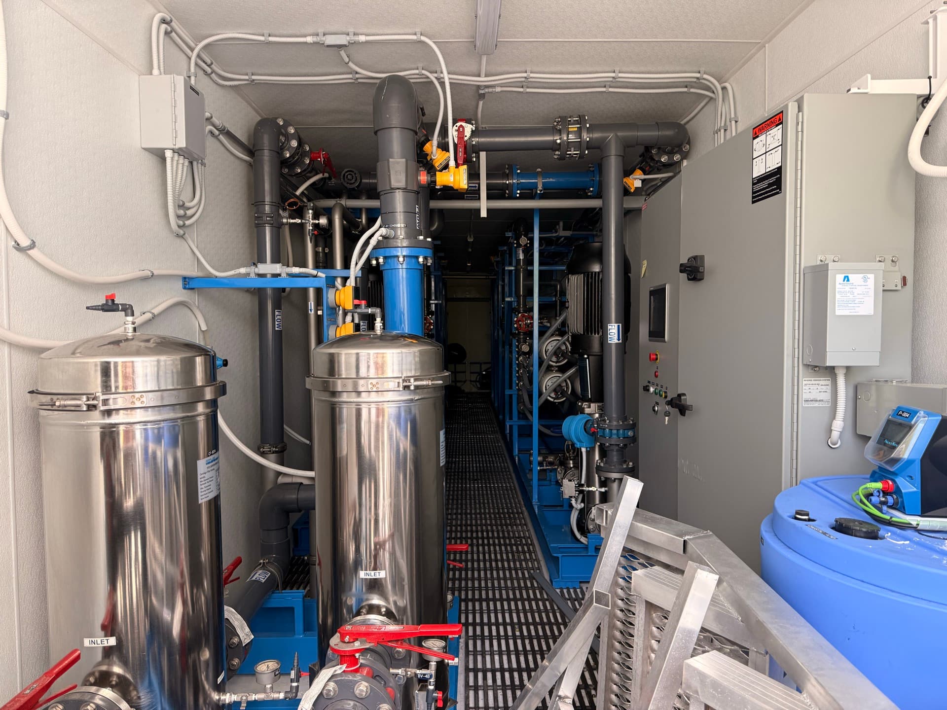 Inside an industrial water treatment facility with stainless steel vessels and blue piping